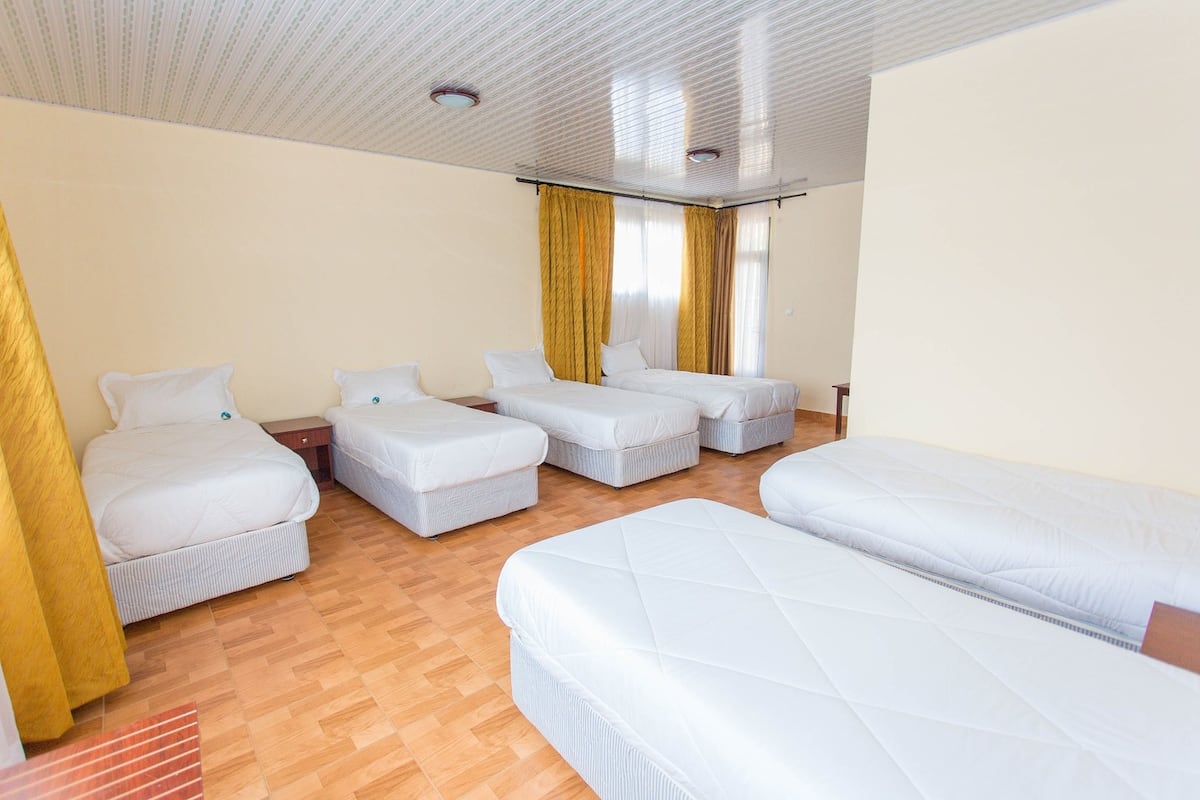 Habitación de hotel con cuatro camas dispuestas en forma de U, suelo de madera e iluminación empotrada en el techo.