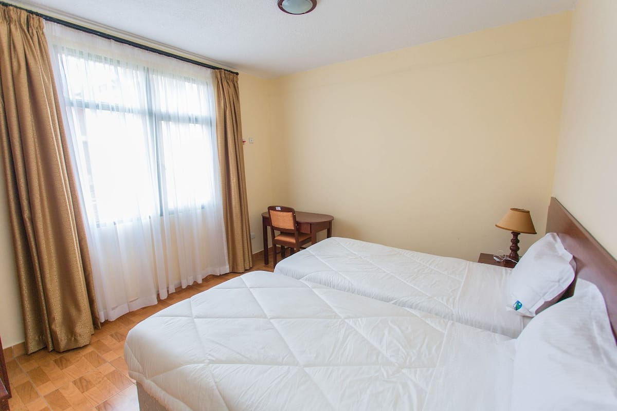 Una habitación de hotel con dos camas, una mesita, una silla y una lámpara.