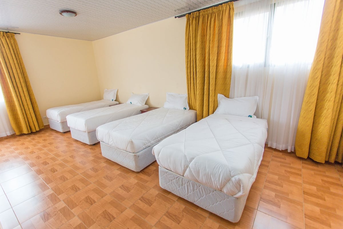 Habitación de hotel con tres camas individuales, suelo de parqué de madera y cortinas amarillas.