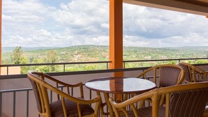 Een balkon met rieten stoelen en een tafel, met uitzicht op een schilderachtig landschap met heuvels en groen.