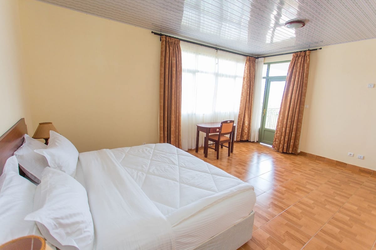 Una habitación de hotel con cama, una silla, una mesa y ventana con cortinas.