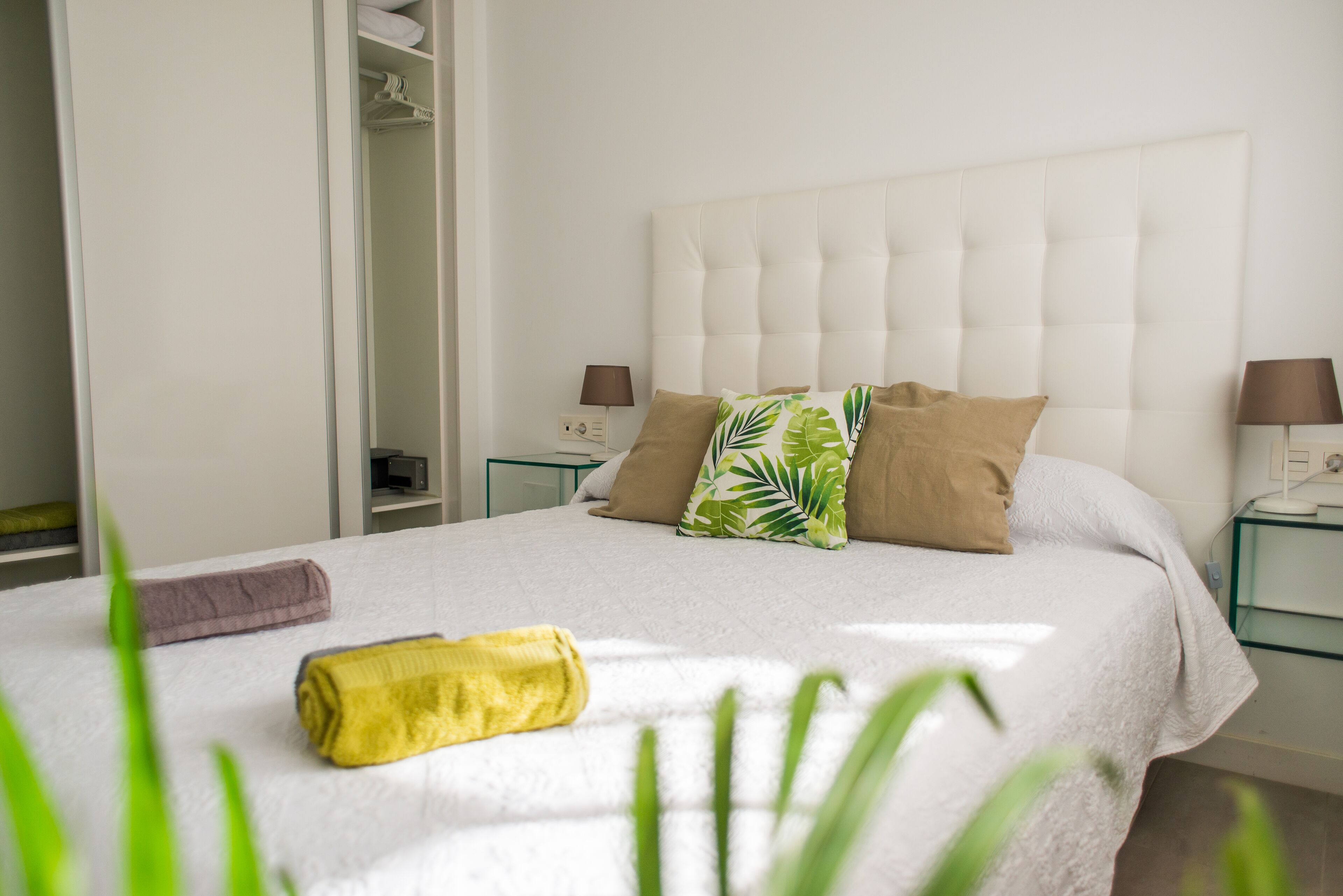 A neatly made bed with a white duvet, two pillows, and a rolled towel.