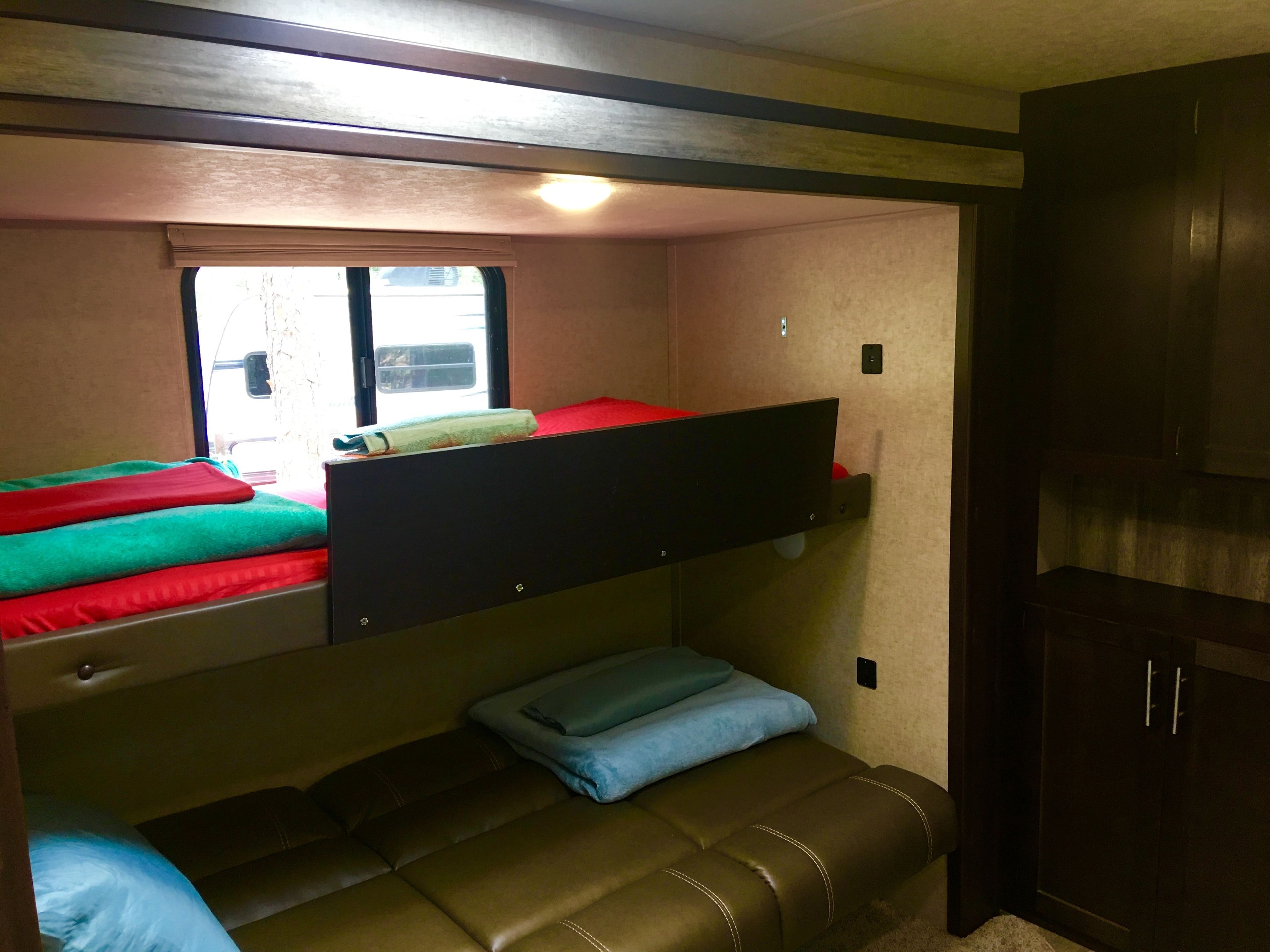 A compact RV interior with a bunk bed, a small sofa, and a window providing natural light.