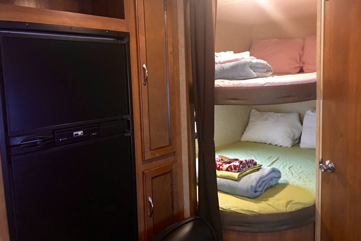 A compact room with a bunk bed, a small desk with a computer, and a wardrobe.