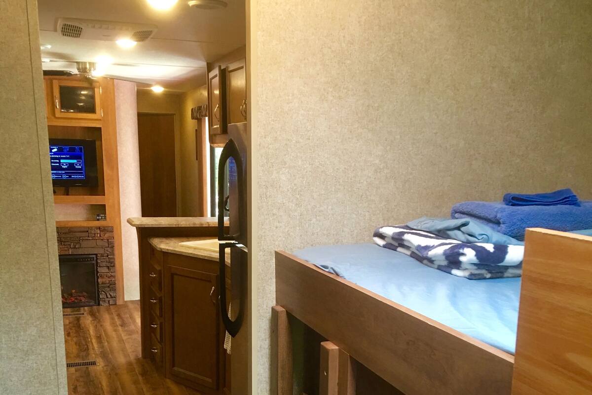 A compact, well-lit room with a bunk bed, a small kitchenette, and a television.