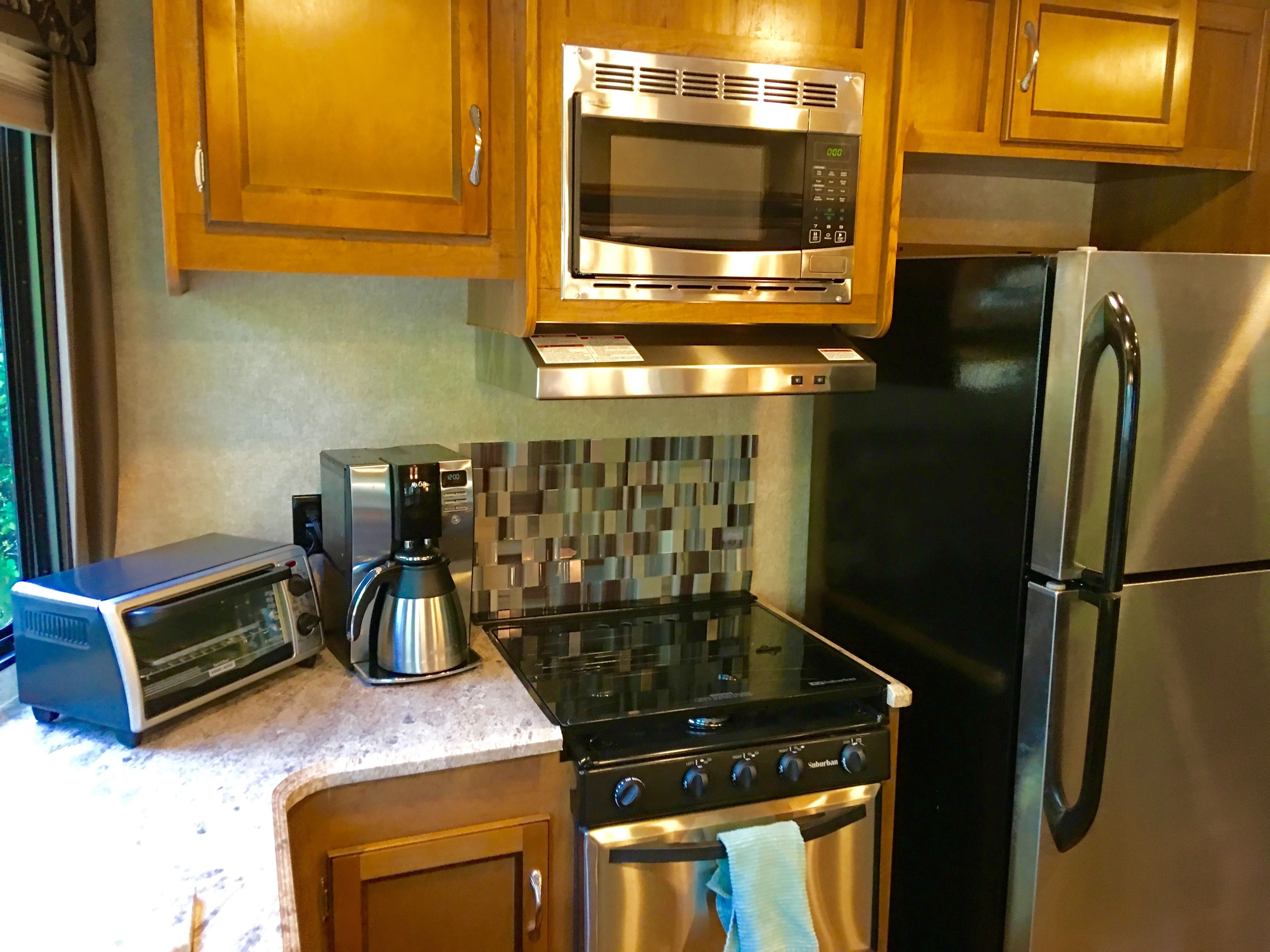 A kitchen with wooden cabinets, a stainless steel microwave, a gas stove, and a refrigerator.