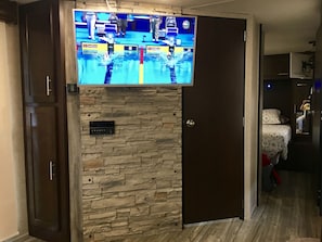 Una stanza con una parete in pietra, una televisione montata sopra e una porta che dà su un'altra stanza.