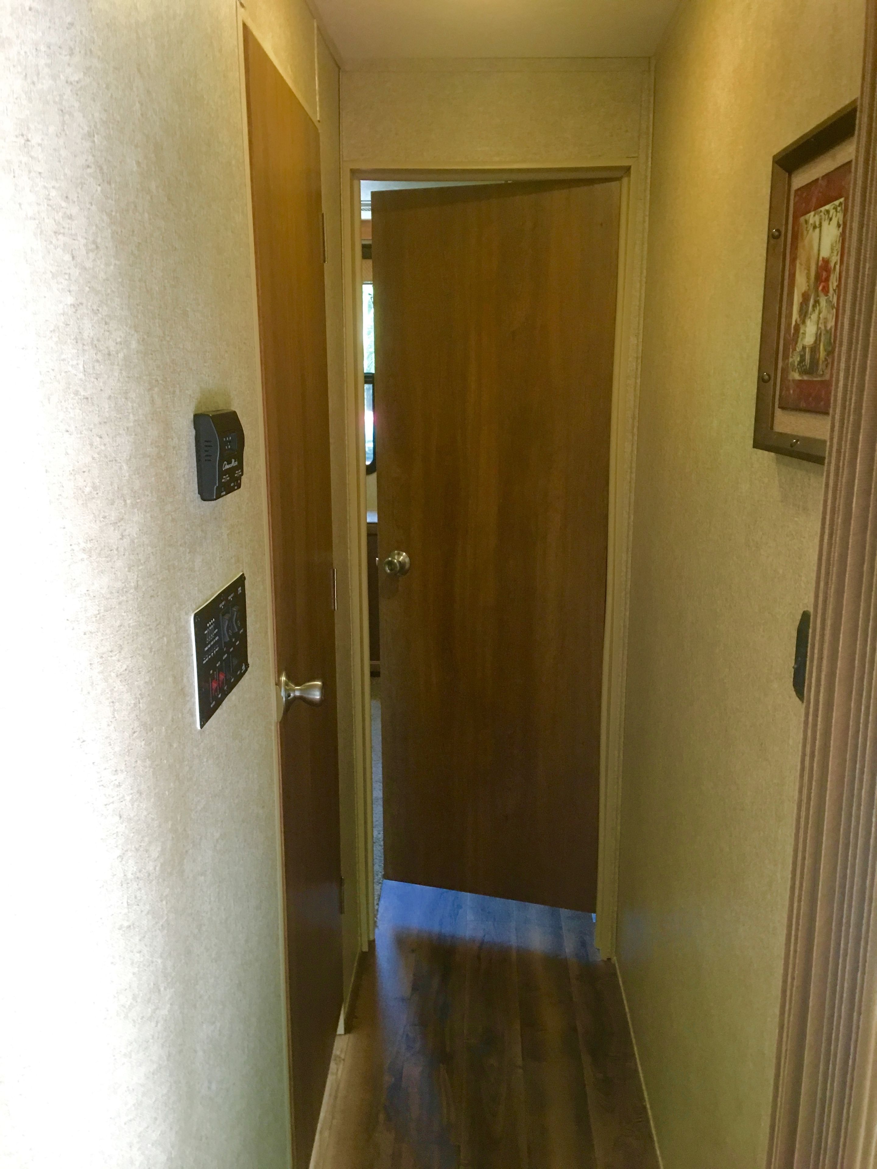 A narrow hallway with a wooden door at the end, a wall-mounted intercom, and a framed picture.