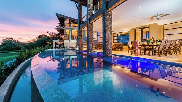 Ein modernes Haus mit großem Pool, Steinpfeilern und einer Essecke mit Sitzgelegenheit im Freien.