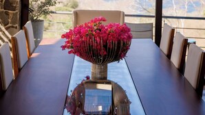 Ein Esstisch mit einer Vase voller pinkfarbener Blumen, einer Glasplatte und hängenden, kugelförmigen Lampen.