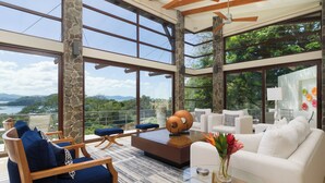 Ein modernes Wohnzimmer mit einem großen Panoramafenster, einem weißen Sofa, blauen Sesseln und einem Couchtisch mit einem Blumenarrangement.