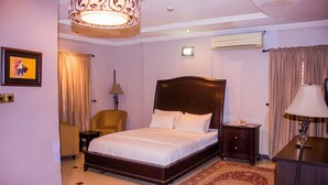 Una habitación de hotel con una cama grande, una silla, una mesita de noche, una lámpara y un cuadro en la pared.
