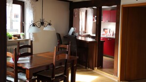 Une table à manger en bois, avec des chaises, un lustre et une vue sur une cuisine aux armoires rouges.