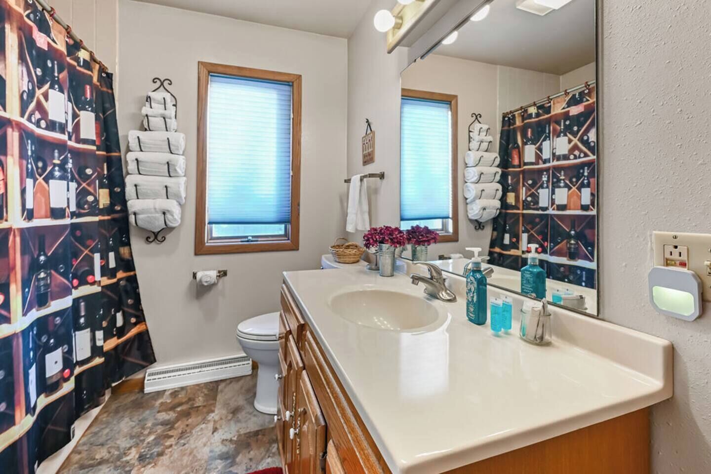A bathroom with a large mirror, a sink, and a toilet. There are towels hanging on hooks and a basket with flowers on the counter.