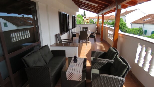 A covered balcony with wicker furniture, a table with a polka dot tablecloth, and a bottle of wine.