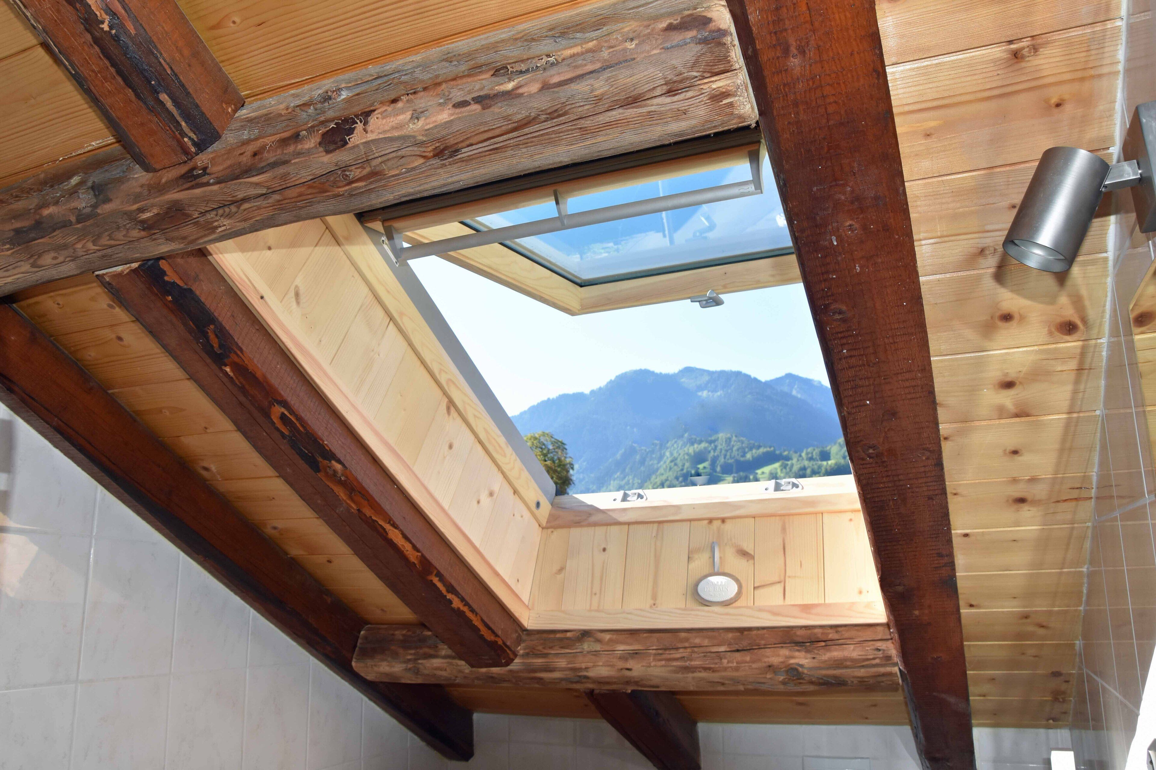 Una habitación de madera con tragaluz, un grifo de agua metálico y vistas a montañas.