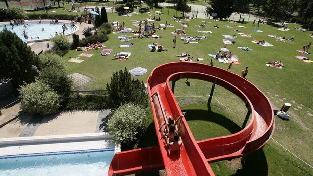 A water slide with a pool at the bottom, surrounded by a grassy area with people sunbathing and a baseball field in the background. - Ancienne Fromagerie, a unique chalet, beautifully renovated  in central Samoens  (Samoëns)
