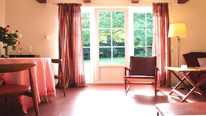 A room with a table set for dining, a chair, a lamp, and a view of greenery outside.