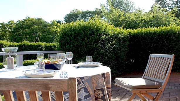 An outdoor dining table set with plates, glasses, and a bowl of fruit.