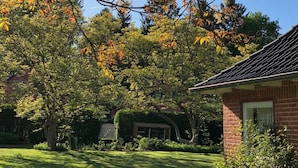 A residential area with a brick house, a well-maintained lawn, and mature trees with autumn foliage.
