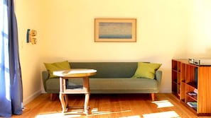 Una sala de estar con un sofá verde, una mesita redonda pequeña, una estantería de madera y un cuadro en la pared.