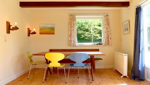 A cozy room with a wooden table, four chairs, a window with floral curtains, a painting, and wall-mounted lights.