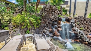 Zona de piscina con sillones, una pequeña cascada y exuberante vegetación tropical.