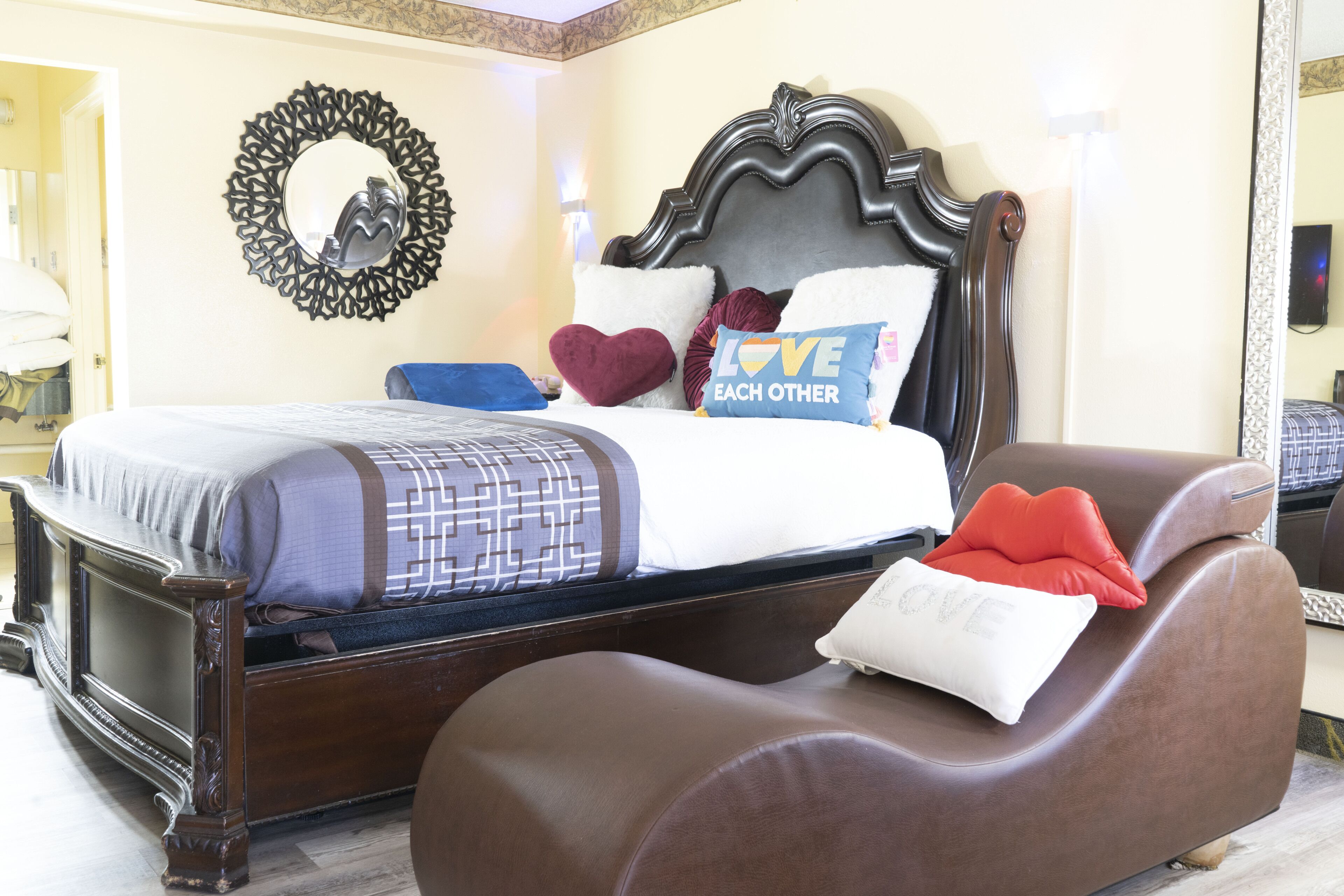 A bedroom with a large bed, a brown leather chair, and a decorative mirror on the wall.
