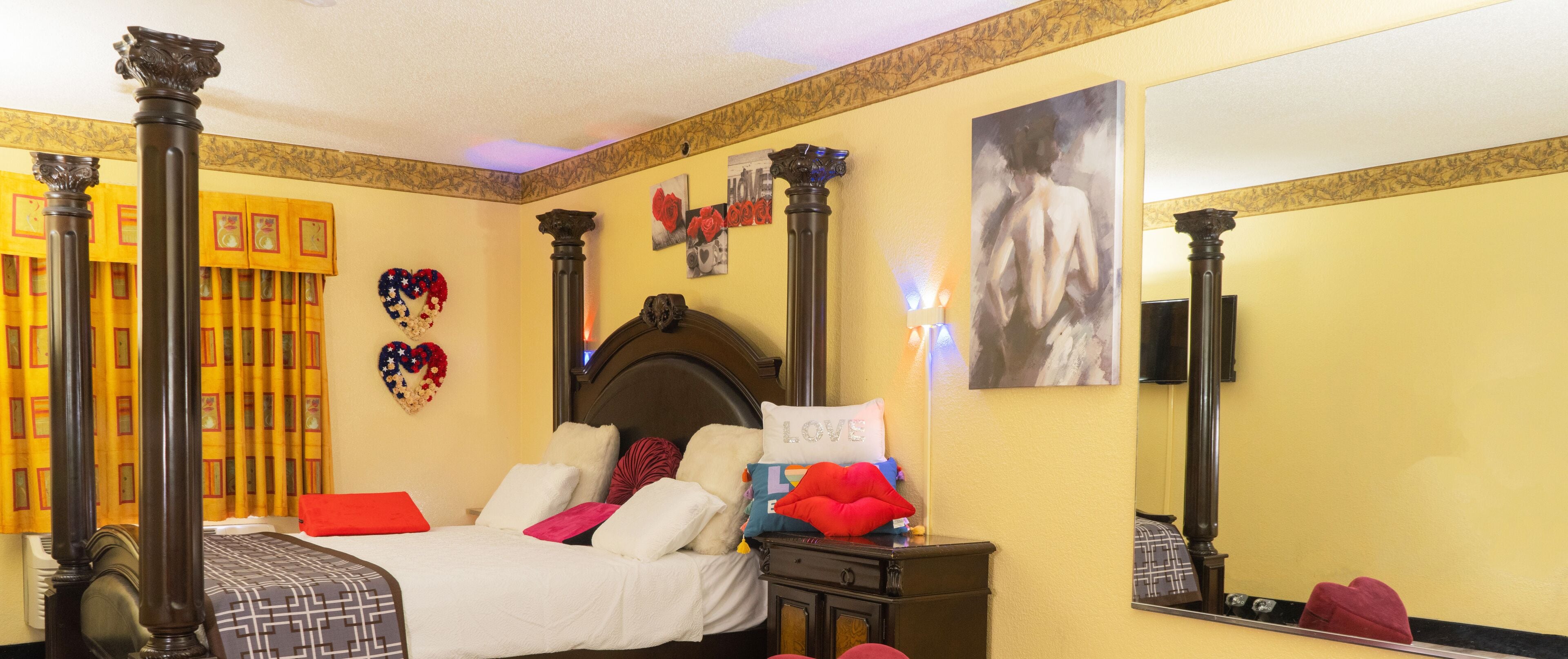 Une chambre d’hôtel avec un lit à baldaquin, une table de chevet, un miroir et des coussins décoratifs.