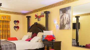 A hotel room with a four-poster bed, a nightstand, a mirror, and decorative pillows.
