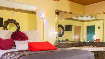 A hotel room with a bed, a large mirror, a television, and a bathroom with a sink and mirror.
