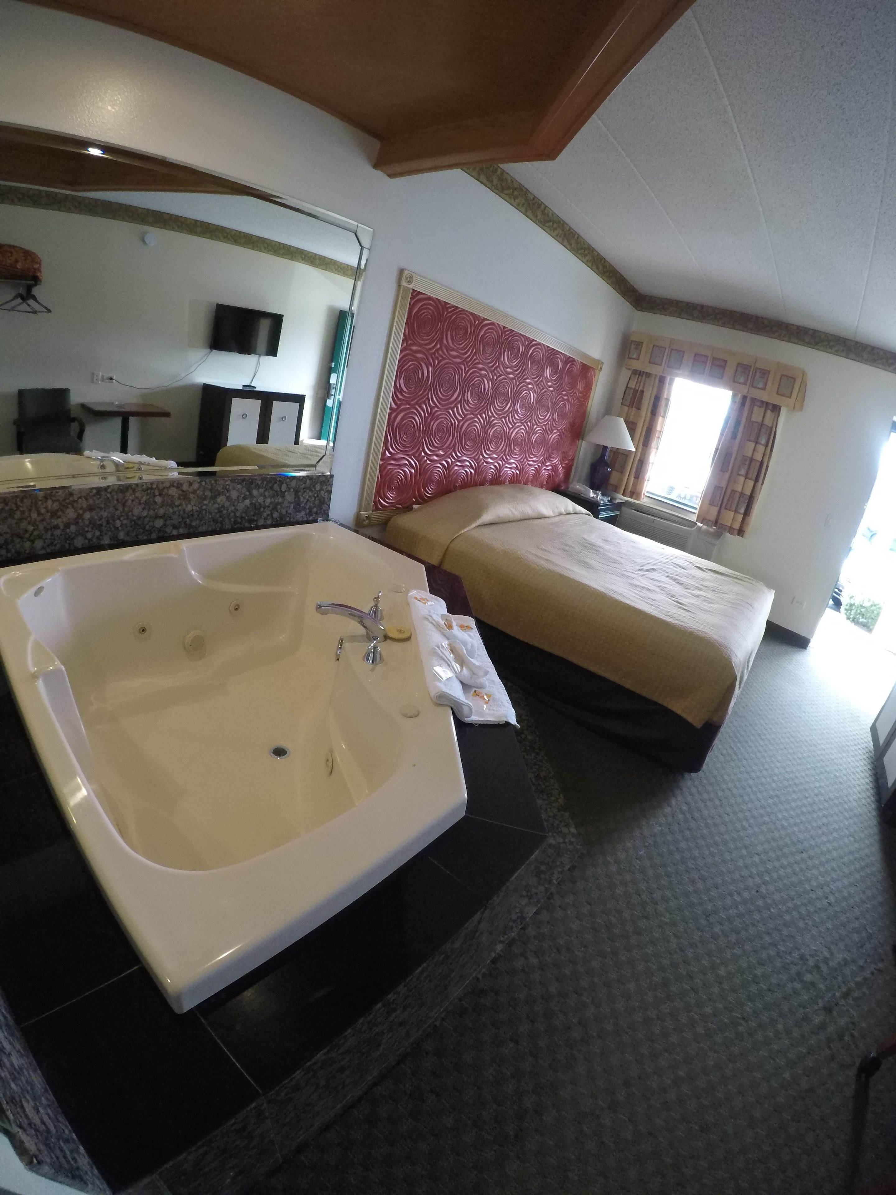 A hotel room with a large bathtub, a double bed, a television, and a desk.