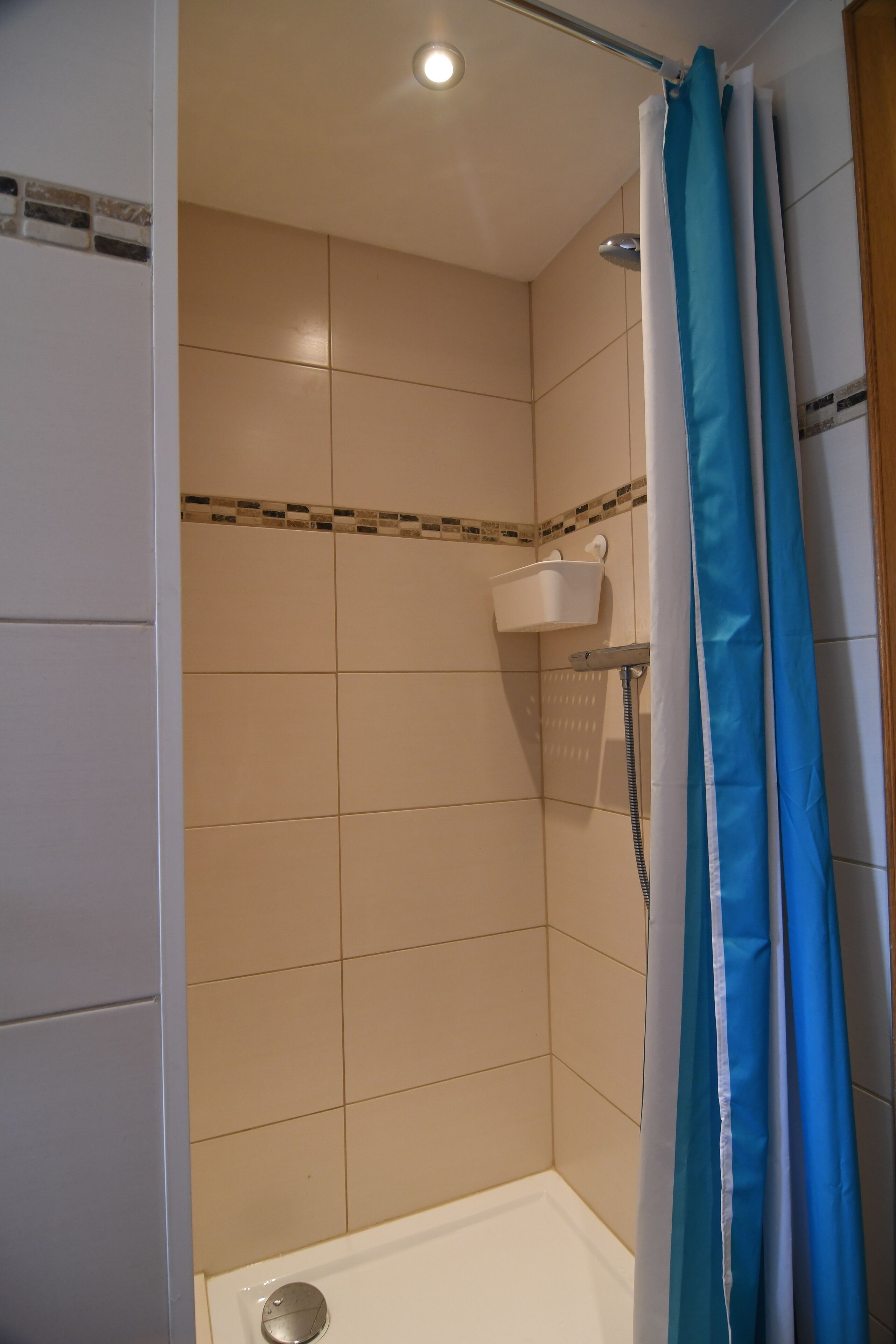 Un espacio de ducha con azulejos color beige, un cabezal de ducha blanco y una cortina de baño azul.