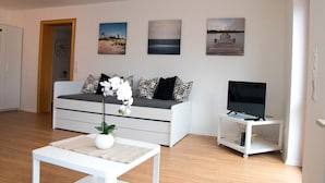 Een moderne woonkamer met een bank, een salontafel met een vaas, een tv op een dressoir en drie schilderijen aan de muur.