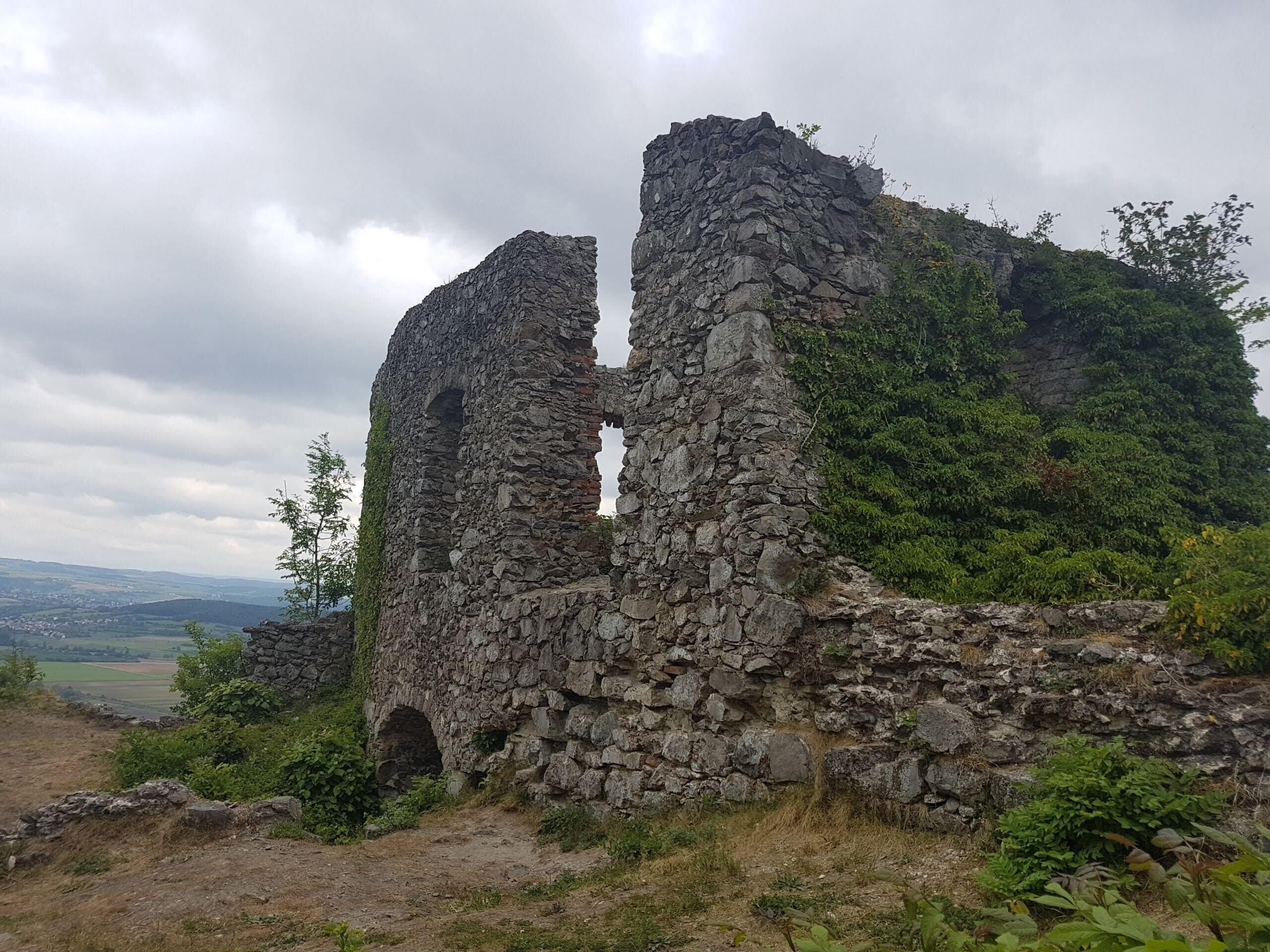 A stone ruin with two arches, surrounded by greenery and a cloudy sky.