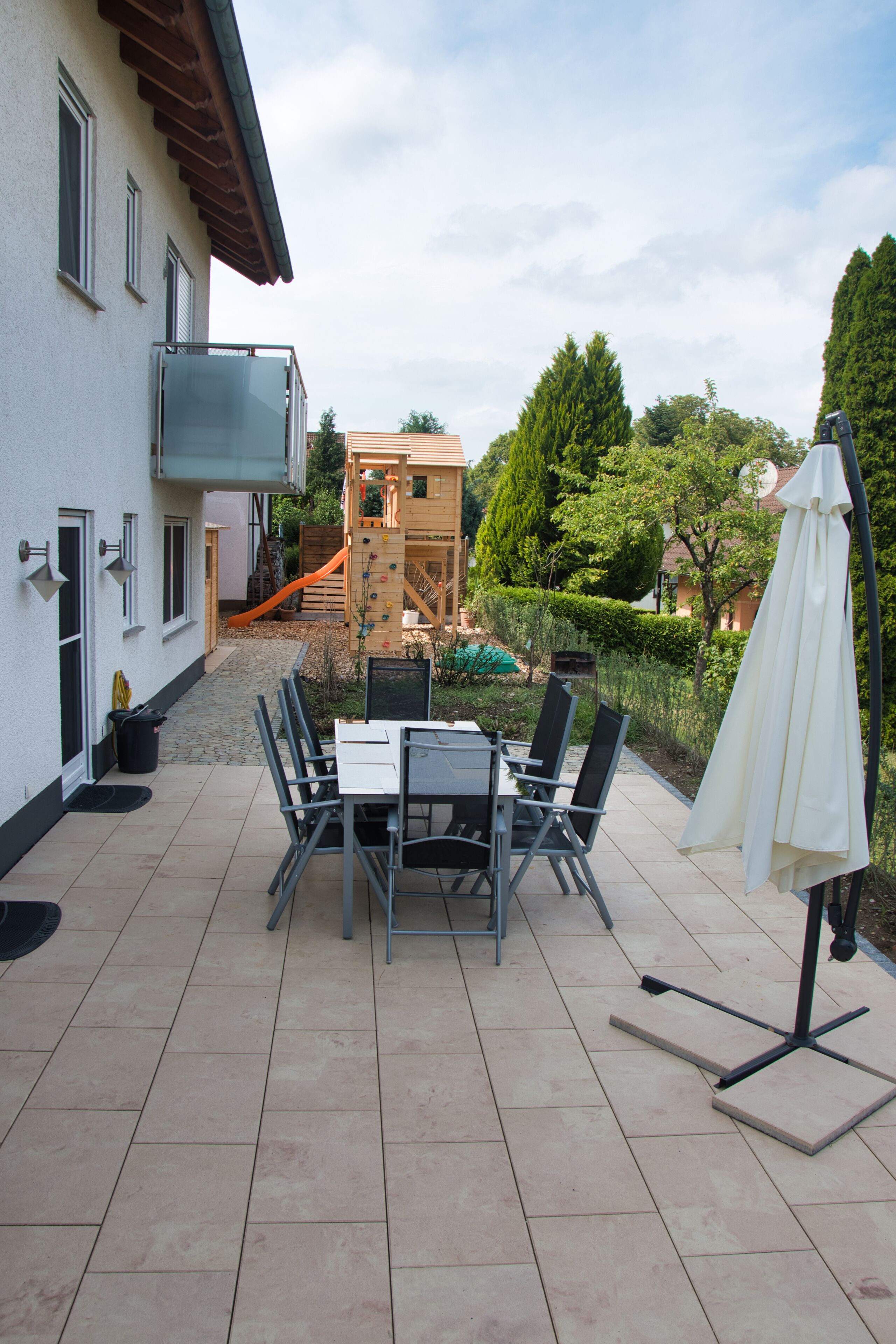 A patio with a table and chairs, a white umbrella, and a play structure in the background.
