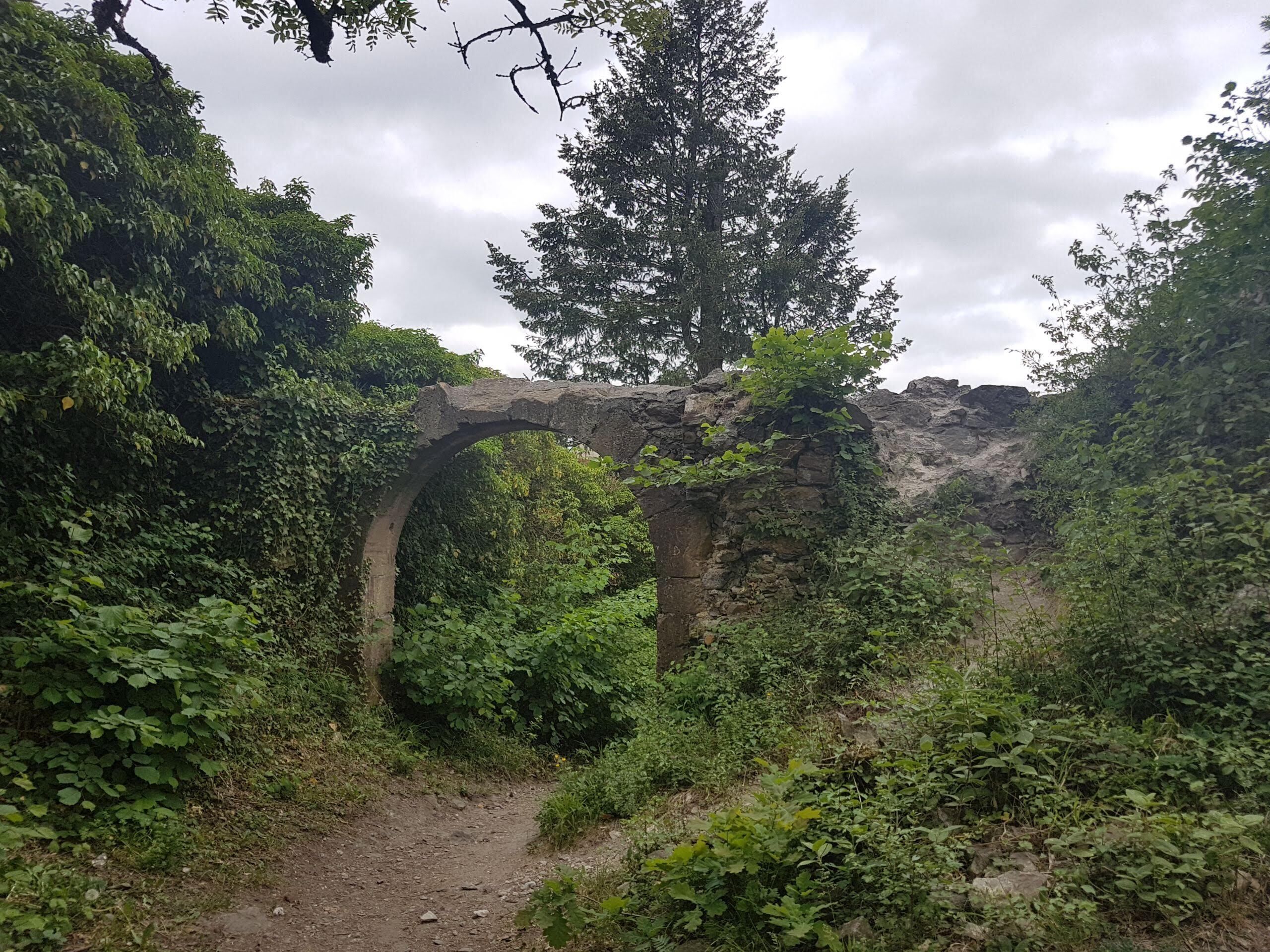 An ancient stone archway surrounded by lush greenery and a dirt path.