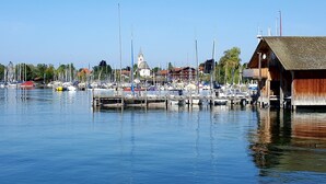 Ein Yachthafen mit mehreren Booten an hölzernen Stegen, eine Kirche mit Kirchturm und ein hölzernes Bootshaus.