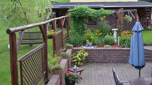 Ein Patio mit Holzlattenzaun, Pflanzkübeln, einer Backsteinmauer und einem Tisch mit blauem Sonnenschirm.