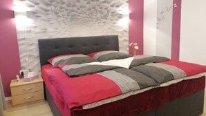 Ein Schlafzimmer im modernen Stil, mit einem Bett mit roter und grauer Bettwäsche, einem dunklen Kopfteil und einer dekorativen Wandverkleidung.