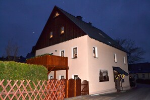 A two-story building with a sloped roof, a wooden porch, and a small garden area. - Modern and spacious, opened in August 2017 Apartment for 4 people (Bärenstein)