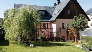 Ein zweistöckiges Haus mit geneigtem Dach, einer Holzterrasse und einem Gewächshaus.