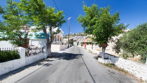 A quiet, tree-lined street with buildings on either side, leading towards a hill. - Mountain view villa !!! (Karpathos)