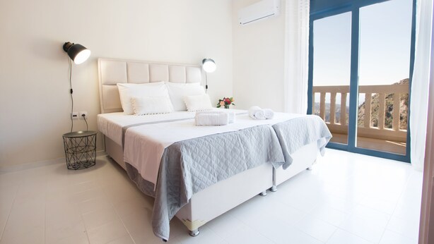 A bedroom with a large bed, two bedside lamps, a small side table, and a view of the outdoors through a balcony. - Mountain view villa !!! (Karpathos)