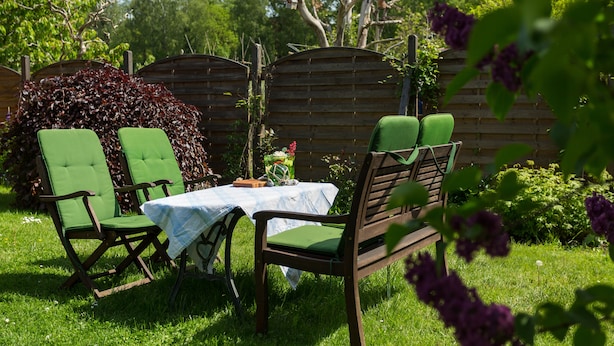 A garden patio with a table and chairs, surrounded by a wooden fence and lush greenery. - "Kleine Küstenpause" - Apartment in the outbuilding (Wlan) (Garz/Rügen)