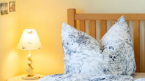 A bedroom with a wooden headboard, a bed with patterned bedding, a bedside lamp, and a wall with framed pictures. - "Kleine Küstenpause" - Apartment in the outbuilding (Wlan) (Garz/Rügen)