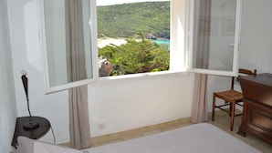 A room with a large window offering a view of a beach and greenery.