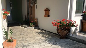 Een verhard pad dat leidt naar een gebouw, met plantenbakken en een houten brievenbus.