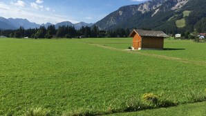 Een landelijk landschap met een houten gebouw, een heldere lucht en bergen op de achtergrond.