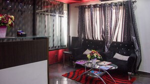 Ein modernes Wohnzimmer mit Glastrennwand, einem schwarzen Sofa, einem kleinen Tisch mit Büchern und einer Blumenvase sowie einem Teppich in Rot und Schwarz gestreift.